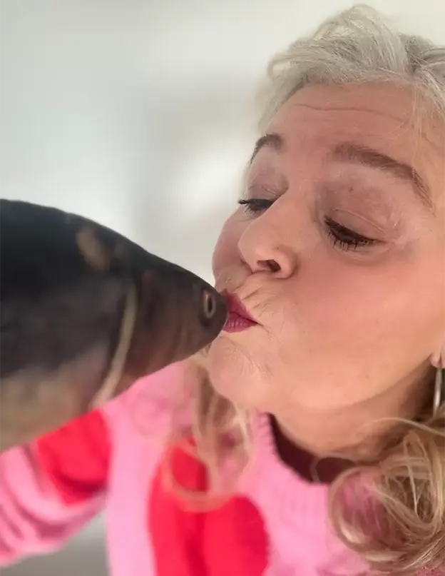 Eine Frau mit hellem Haar küsst einen schwarzen Hund auf die Lippen und genießt den Moment, als würde man eine Rente planen.