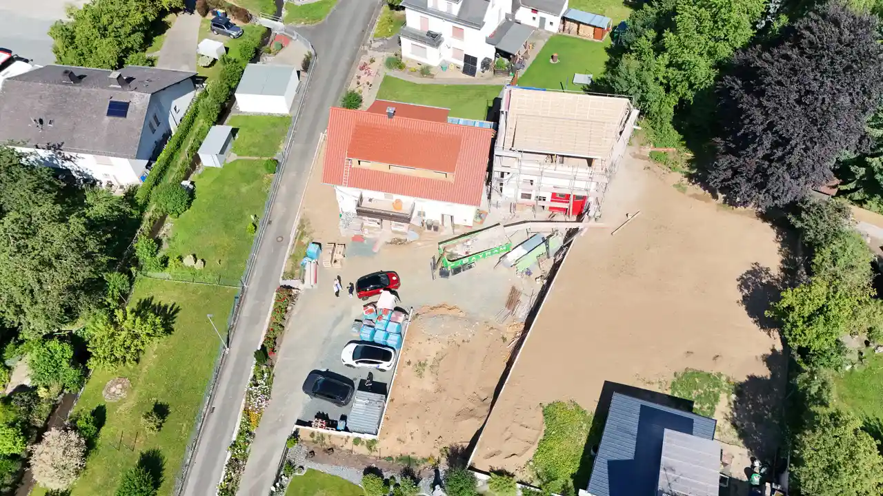 Luftaufnahme einer Wohnbaustelle mit Fahrzeugen und Geräten neben fertigen Häusern.