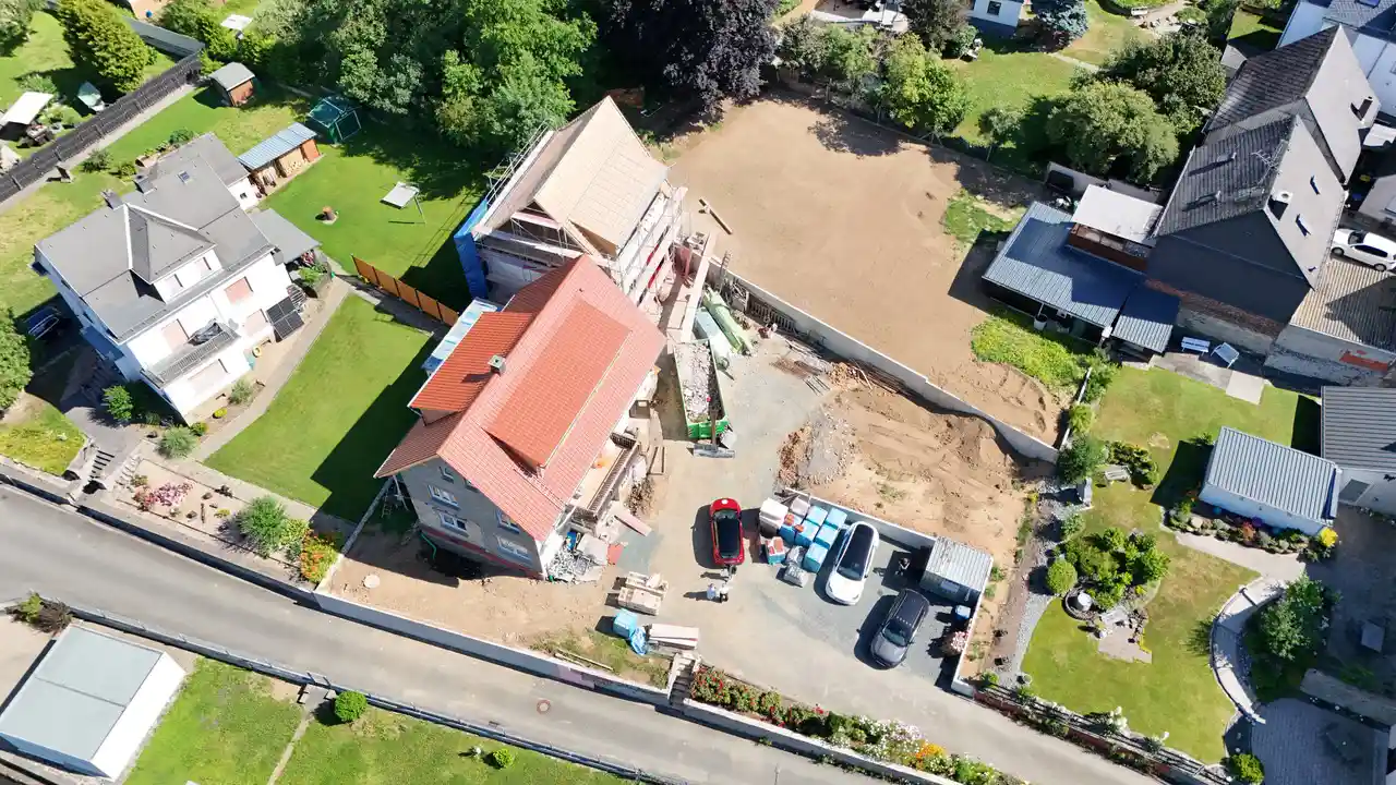 Luftaufnahme eines im Bau befindlichen Hauses mit in der Nähe geparkten Autos und umliegenden grünen Rasenflächen.