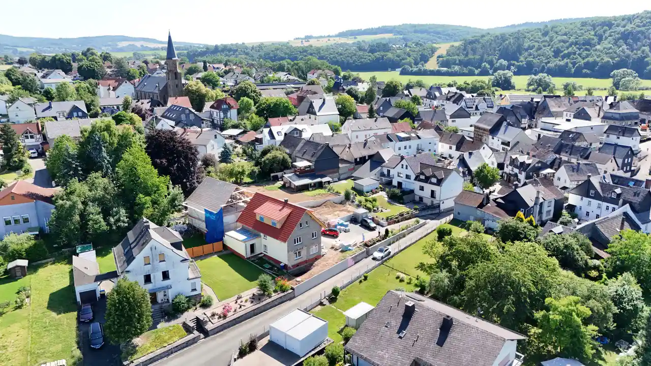 Luftaufnahme des kleinen Dorfes, in dem die Senioren-Wohngemeinschaft entstehen wird. Häuser, Straßen, Grünanlagen und eine Kirche, im Hintergrund bewaldete Berge.