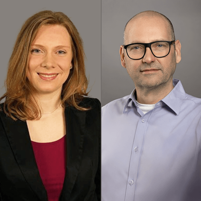 Eine Frau in einem schwarzen Blazer und ein Mann mit Brille und hellem Hemd sind nebeneinander vor einem schlichten Hintergrund abgebildet.