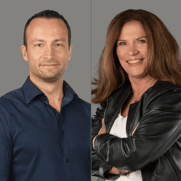 Ein Mann in einem dunklen Hemd und eine Frau in einer schwarzen Jacke posieren nebeneinander vor einem grauen Hintergrund.