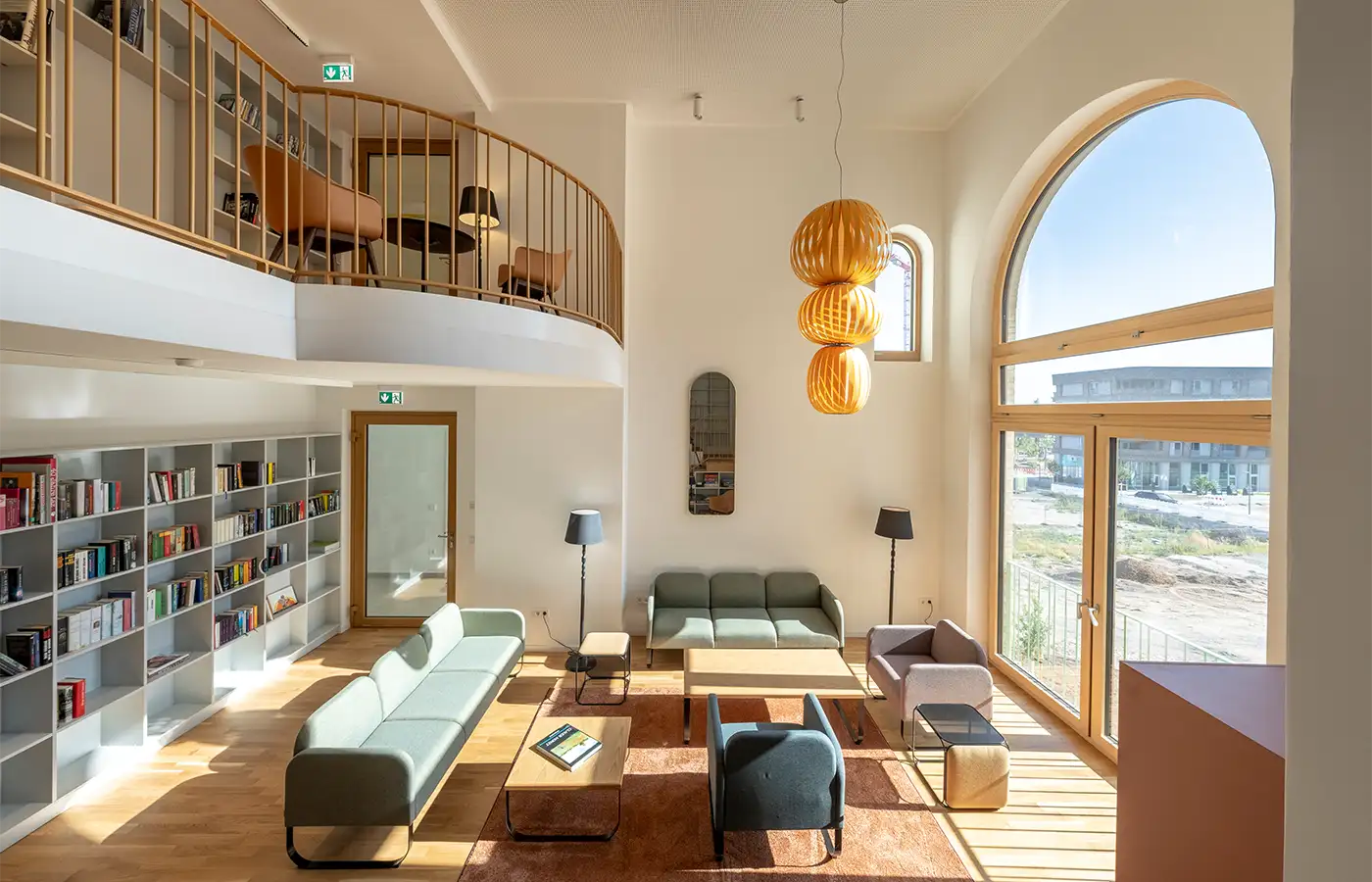 Gemeinschaftsraeume-Kaminzimmer-ANUNDO Modernes Kaminzimmer mit Sofas, Bücherregalen, großem Bogenfenster, Sitzgelegenheiten im Zwischengeschoss und Pendelleuchte.