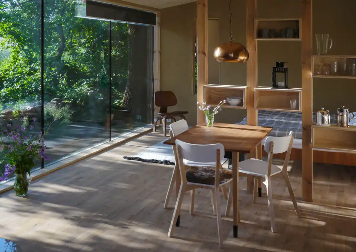 Wohndorf-Re-hof-Raum Moderner Essbereich mit Holzmöbeln, großen Glasfenstern und Blick auf die grüne Umgebung.