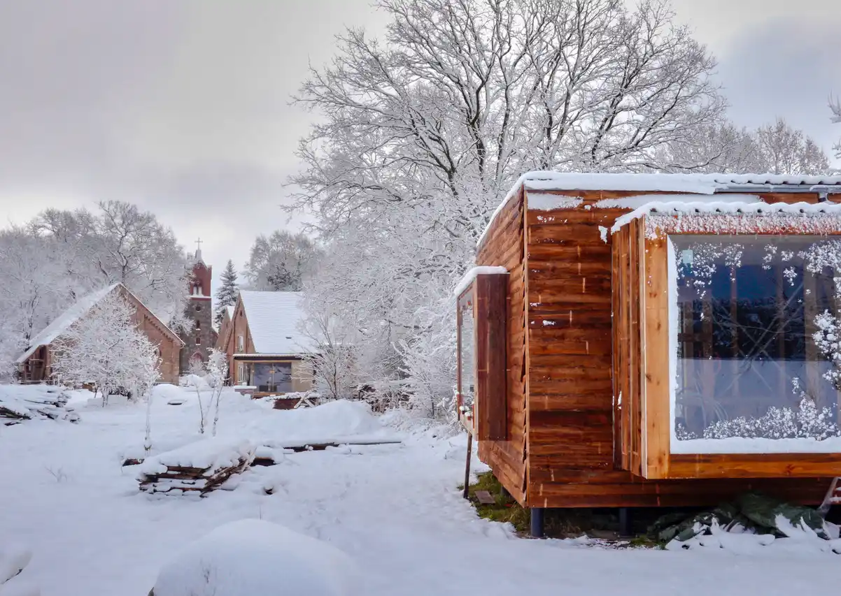 Wohndorf-Re-hof-Winter Holzhütten umgeben von schneebedeckten Bäumen und Boden an einem bewölkten Wintertag.