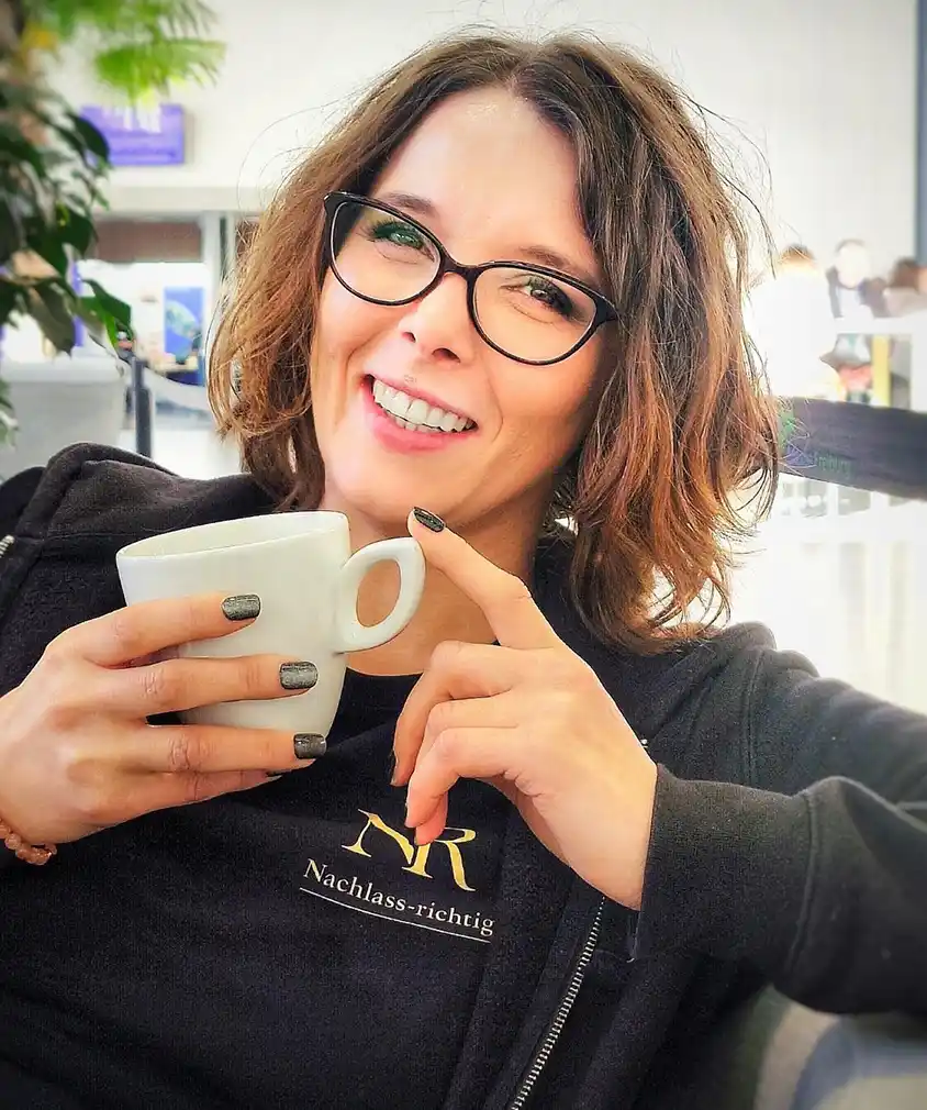 Frau mit Brille, lächelnd und mit Kaffee in der Hand, vielleicht über Vermögen nachdenkend oder ihr Testament im Haus planend.