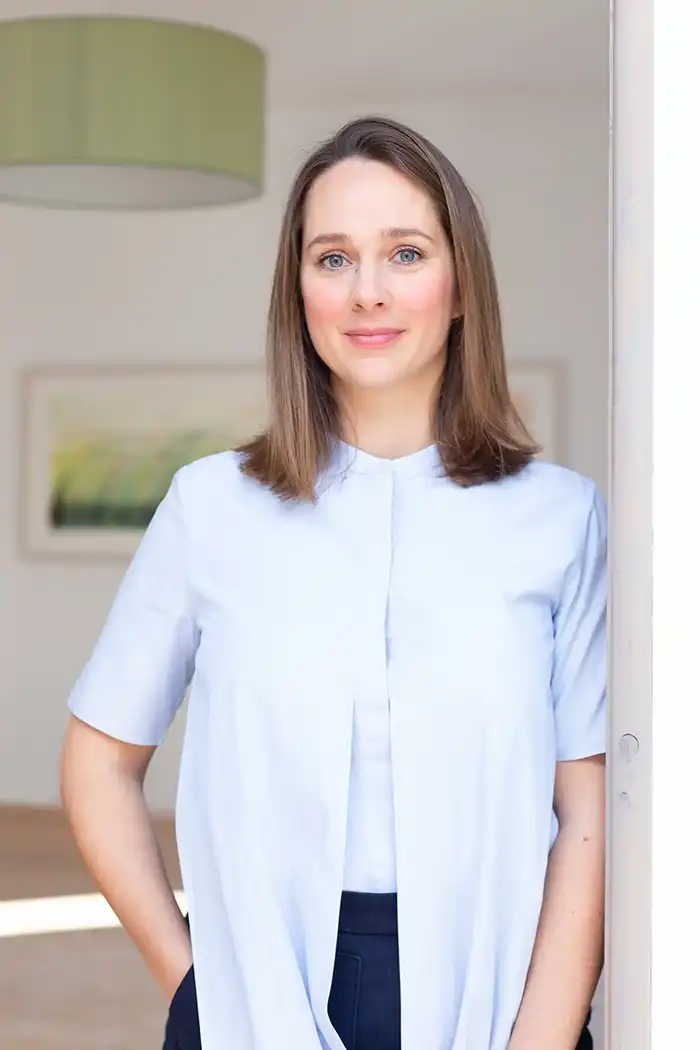 Franziska-Rauch_Yorokani Eine Frau mit schulterlangem braunem Haar trägt ein hellblaues „Magnetkleidung Yorokani“-Shirt und steht neutral in einem Raum.