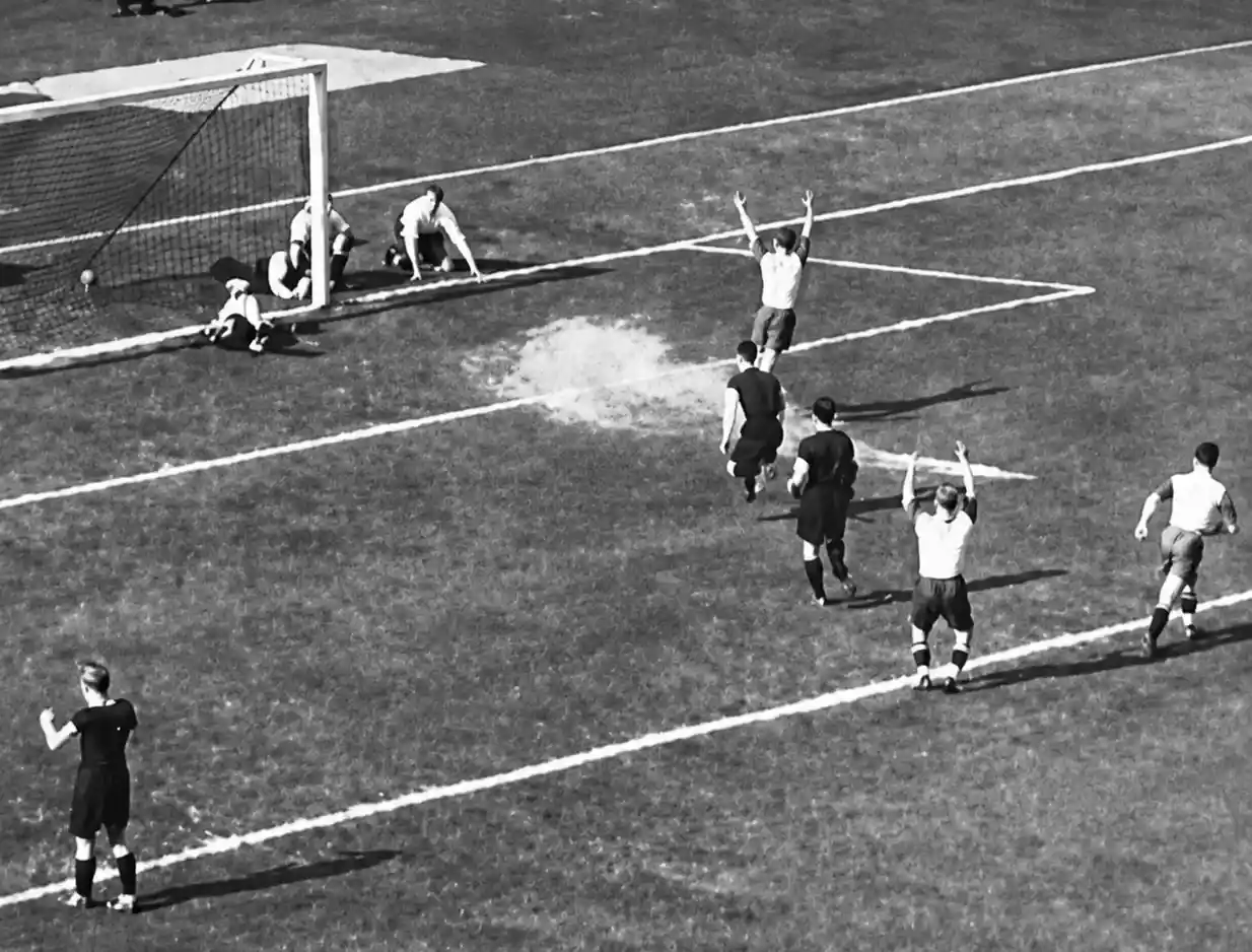 Staubiger-Elfmeter-1932-Oskar-Rohr Fußballspieler feiern ein Tor, während die gegnerischen Spieler auf einer Wiese in der Nähe des Torpfostens sitzen und stehen.