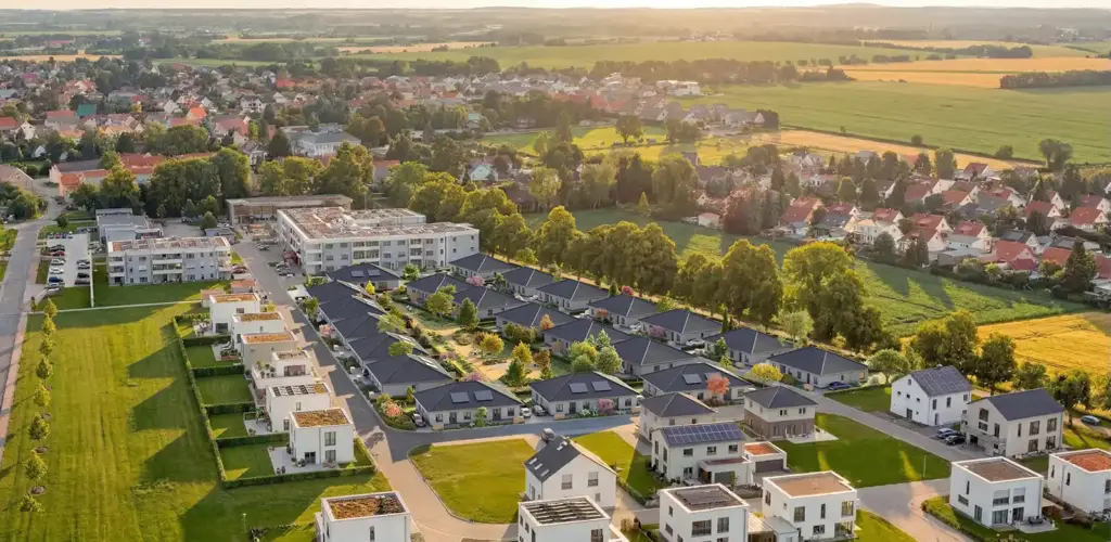 Luftaufnahme eines Vorortviertels mit modernen Häusern, grünen Rasenflächen und umliegenden Feldern bei Sonnenuntergang.