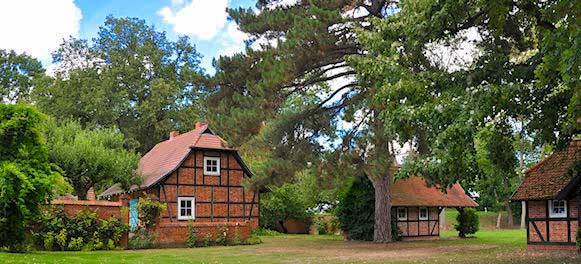 Gutleben-Buettnersdorf-Haus Ziegel- und Holzhäuschen, umgeben von Bäumen und viel Grün unter einem teilweise bewölkten Himmel.