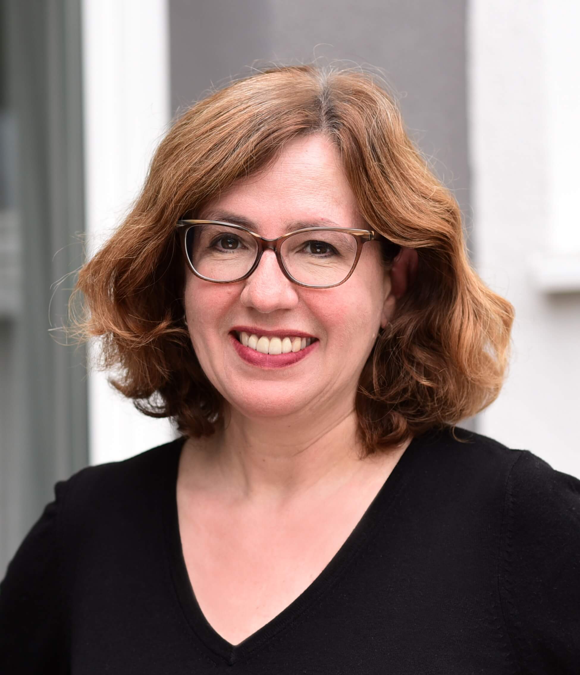 Jeanette-Neidhardt-Rosenberger Nahaufnahme einer Frau mittleren Alters mit schulterlangem braunem Haar und Brille, die in die Kamera lächelt.