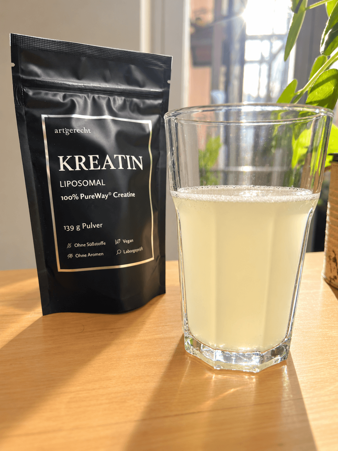 Kreatin-artgerecht-im-glas Ein Beutel mit artgerecht-Liposomen-Kreatinpulver neben einem Glas Mixgetränk.